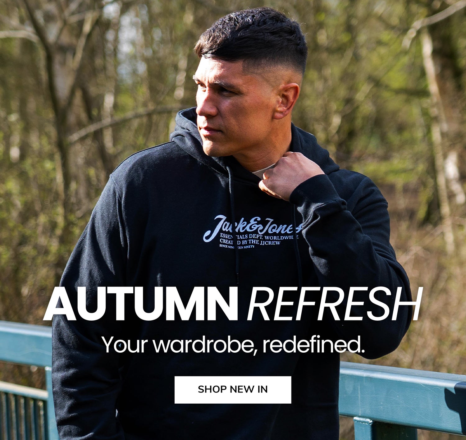 Man wearing a black hoodie with text, standing outdoors with trees in the background